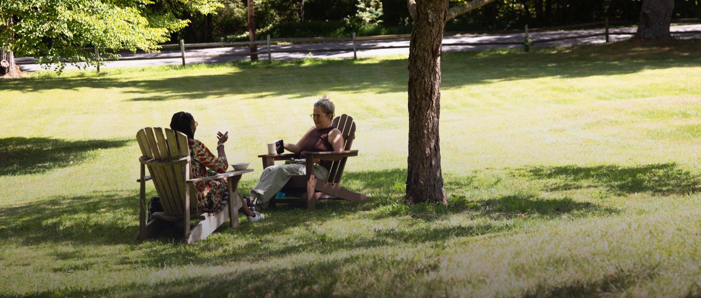 Two women in Adirondack chairs chat under a tree