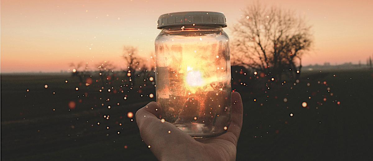 Hand holding a glowing jar at sunset, symbolizing spiritual connection, afterlife communication, and healing from loss.