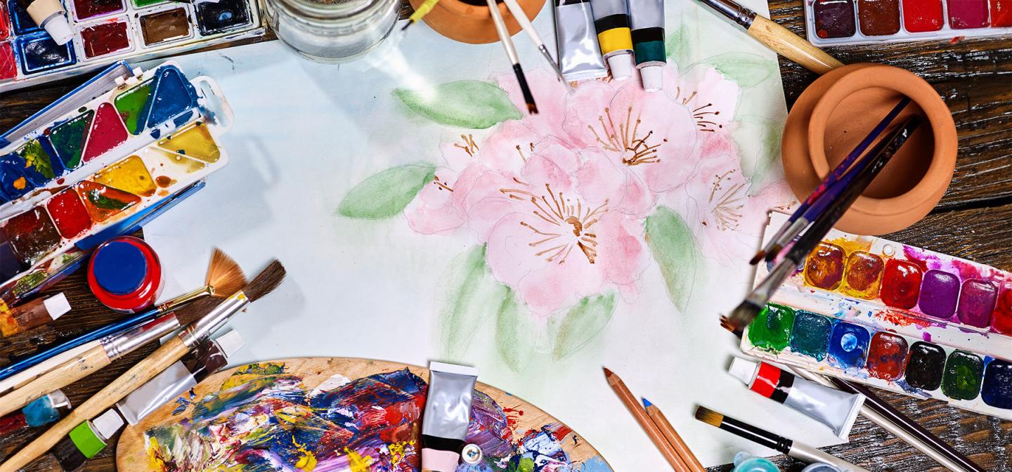 Artist workspace with watercolor painting, brushes, palettes, and art supplies for creative practice.