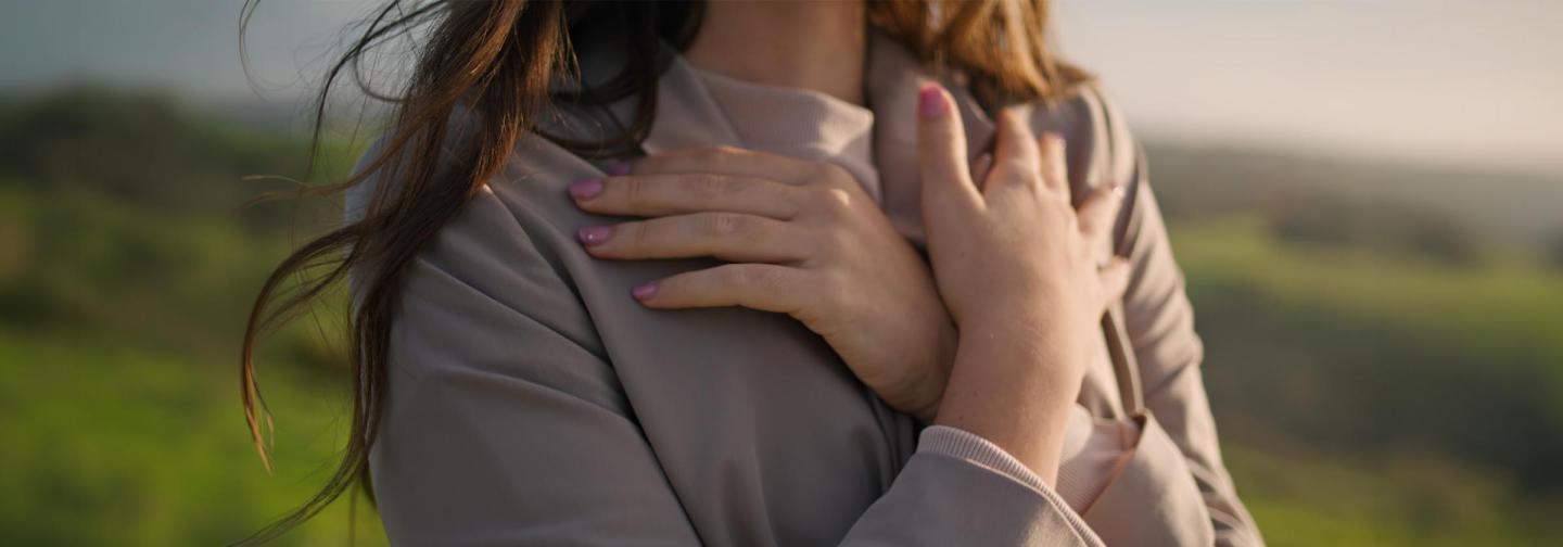 Woman embracing herself outdoors in soft sunlight, symbolizing self-compassion, healing, and recovery from heartbreak.