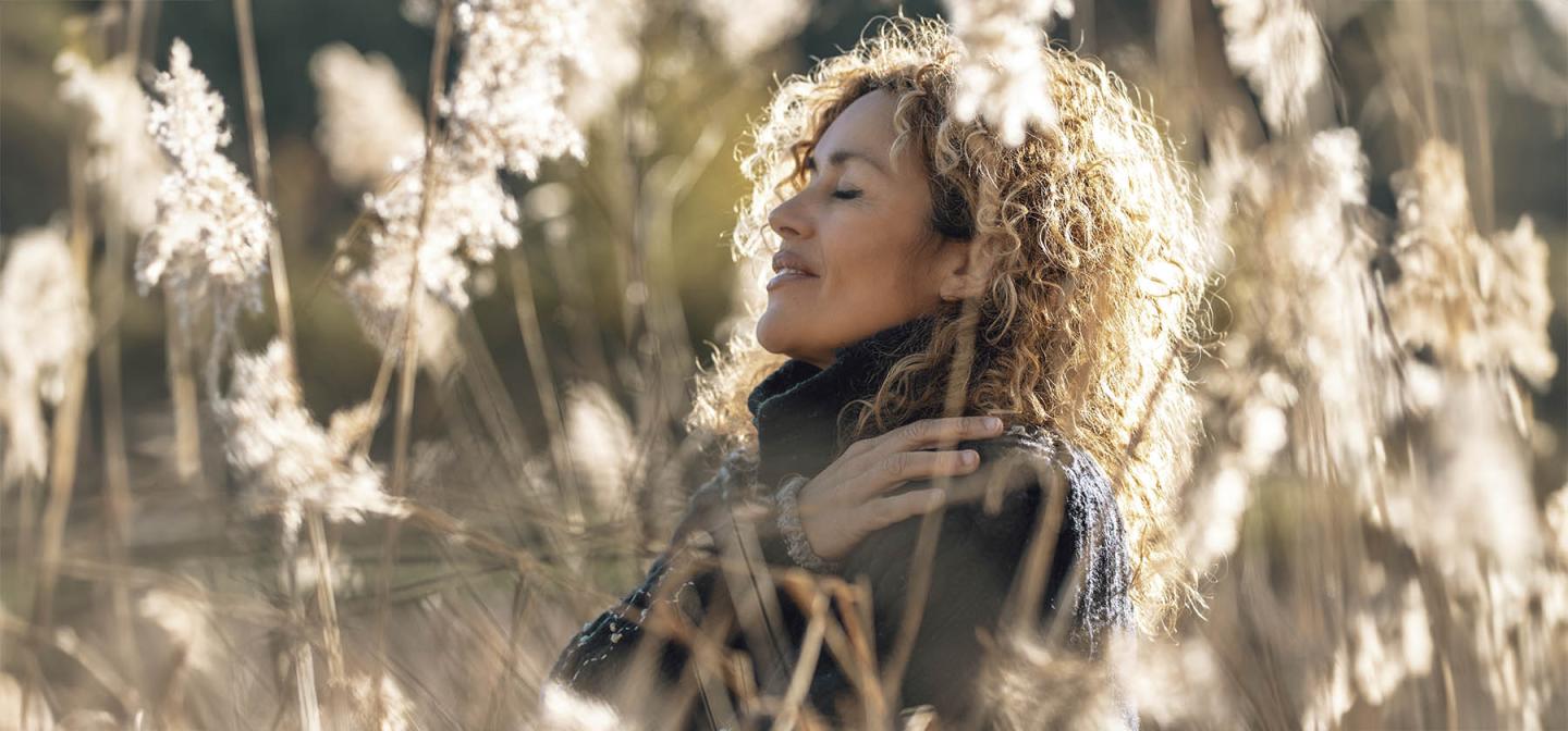 Woman with eyes closed peacefully standing in sunlit tall grass, embracing mindfulness, self-acceptance, and inner peace in nature.