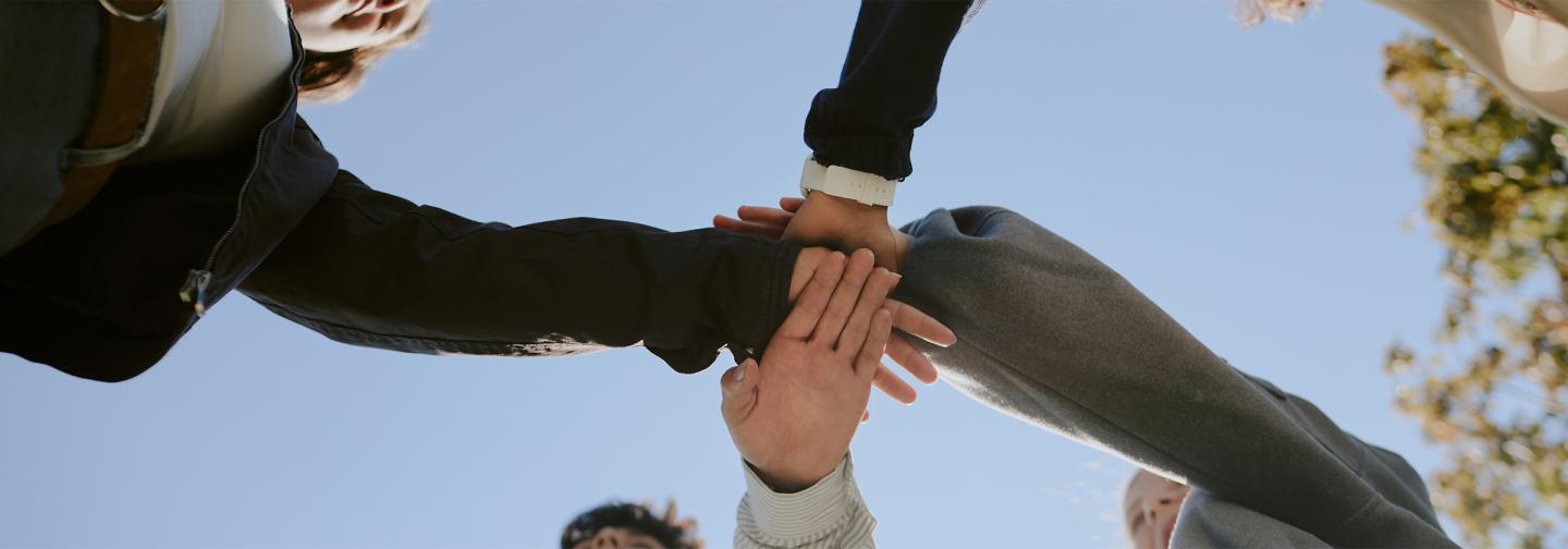People stacking hands in teamwork circle, representing human-centered leadership and collaboration