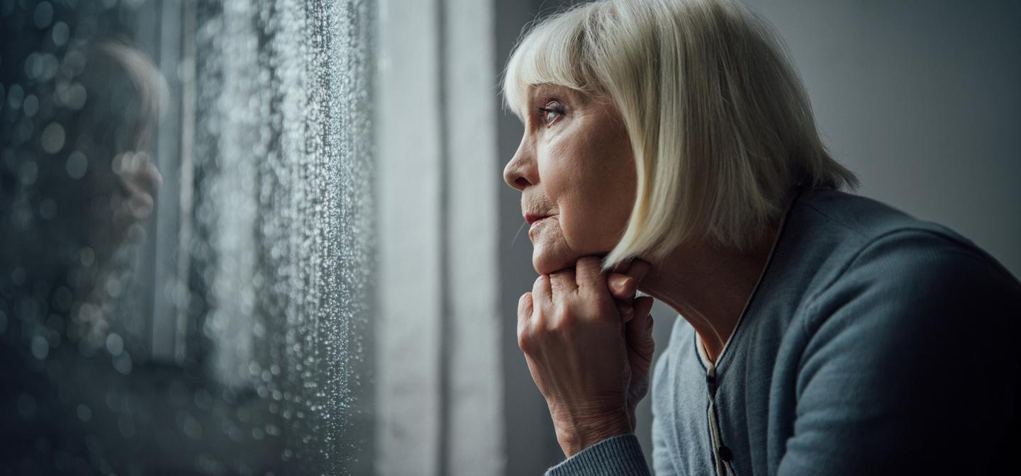 Close-up of woman resting chin on hands, staring out window in contemplation and emotional grief