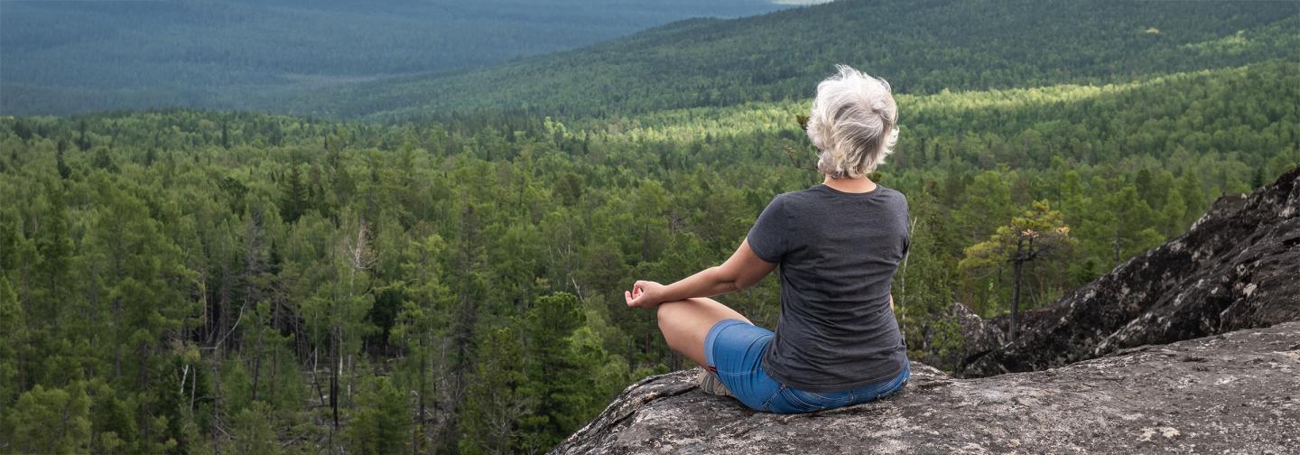 Person meditating on a rocky overlook above forest to reconnect with creativity and nature.