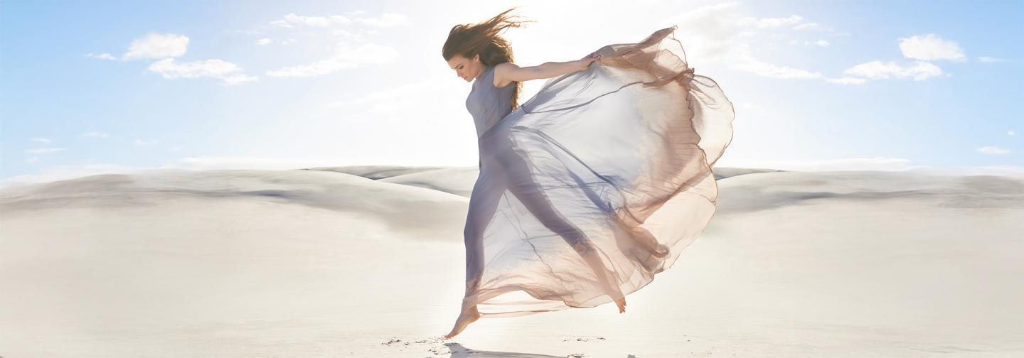 A woman dancing barefoot in a flowing dress on a sunlit desert landscape, symbolizing freedom, joy, and embodied resilience through movement and self-expression.