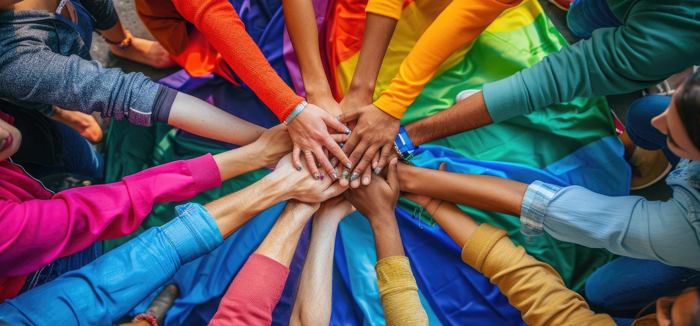 Hands joined over a rainbow flag, celebrating LGBTQ+ unity at Omega’s Pride Weekend.