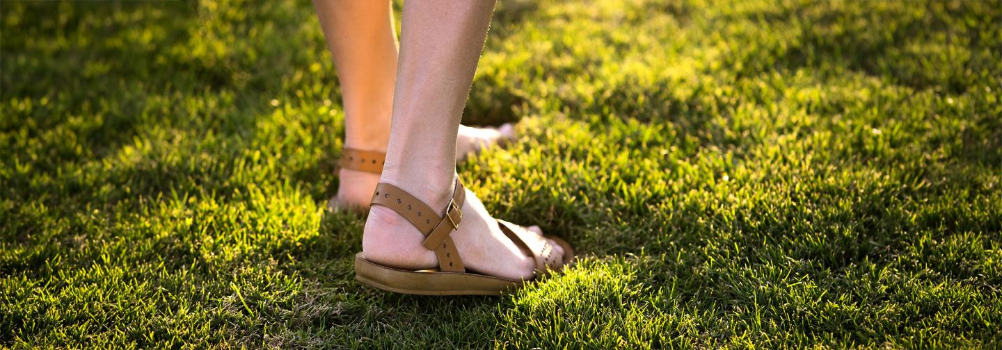 Person standing barefoot on sunlit grass, symbolizing grounding, mindfulness, and calming the nervous system.