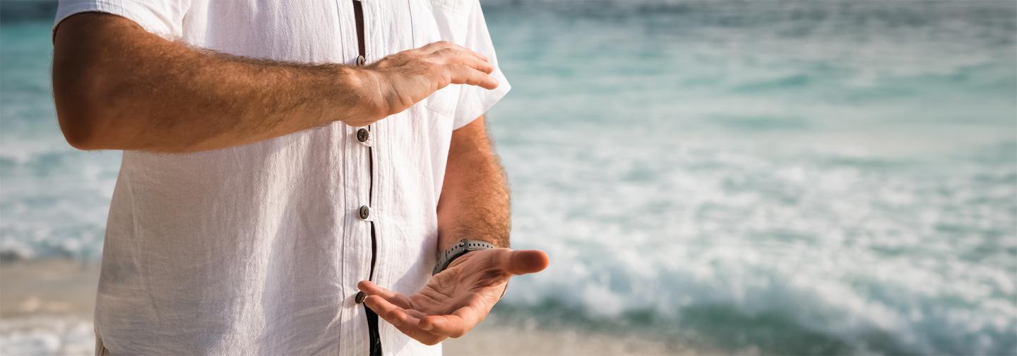Person practicing qi gong by the ocean, moving energy through their body