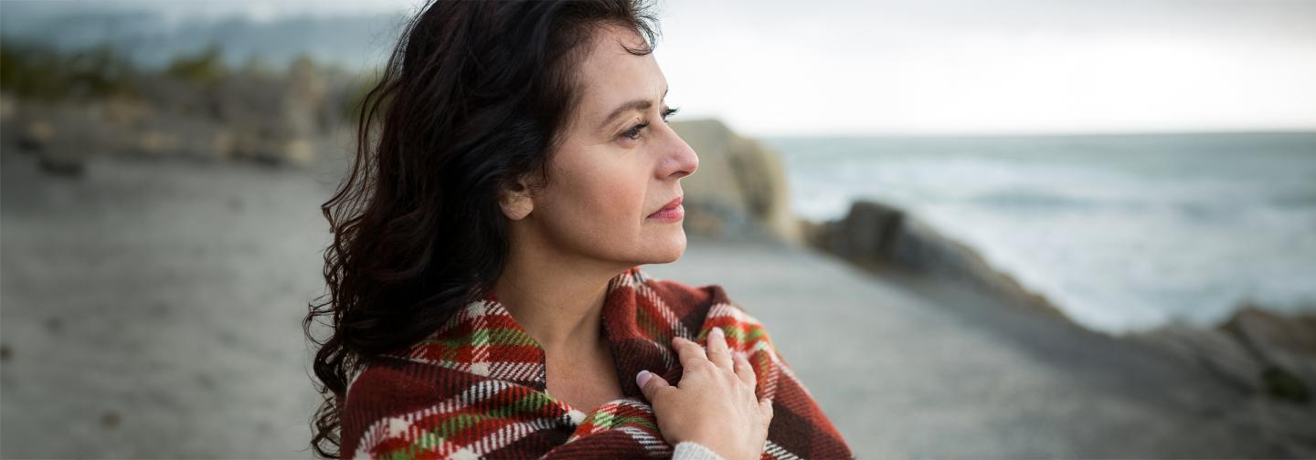 Woman wrapped in a blanket gazing toward the ocean, symbolizing calm, emotional resilience, and healing through Presence Psychotherapy.