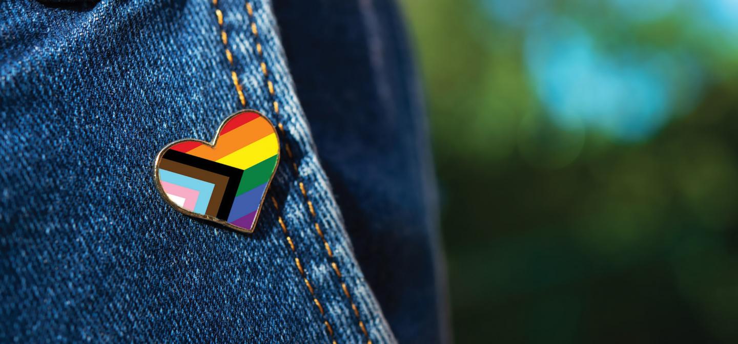Heart-shaped Progress Pride flag pin on denim jacket symbolizing LGBTQIA+ pride, inclusion, and love—celebrating diversity and queer empowerment at Omega Institute’s Pride Weekend.