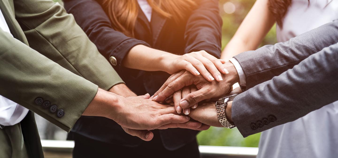 Team members stacking hands to represent collaborative leadership, trust, and shared purpose.