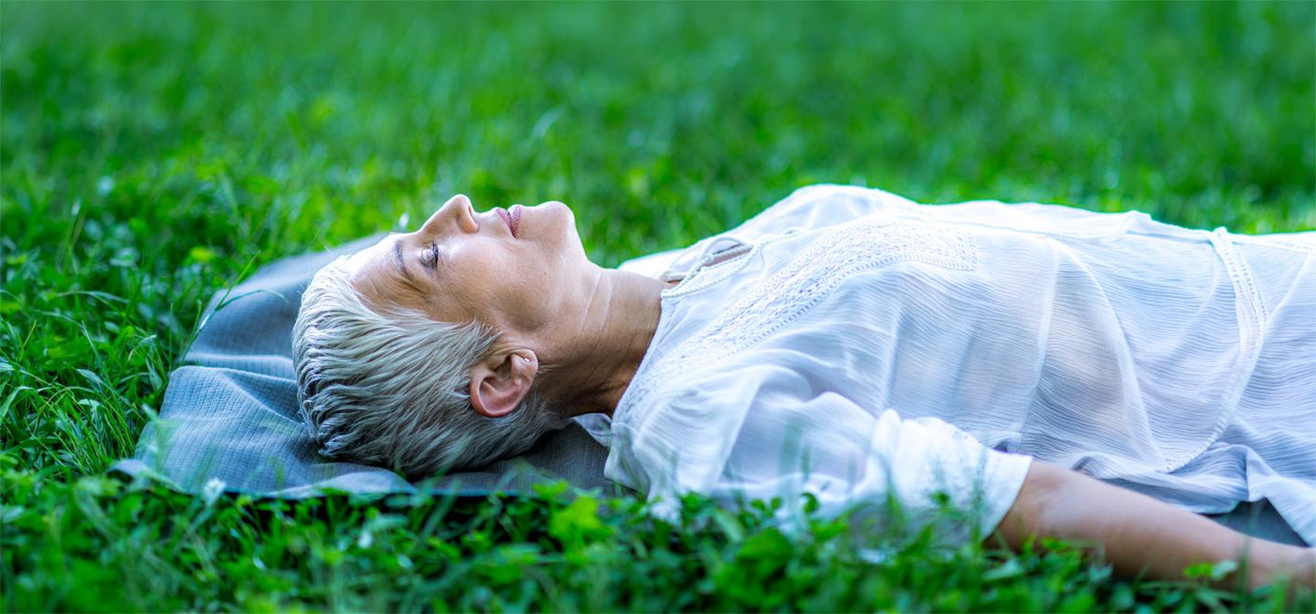 Woman resting outdoors on a mat in grass, representing deep sleep, relaxation, and restorative practice.