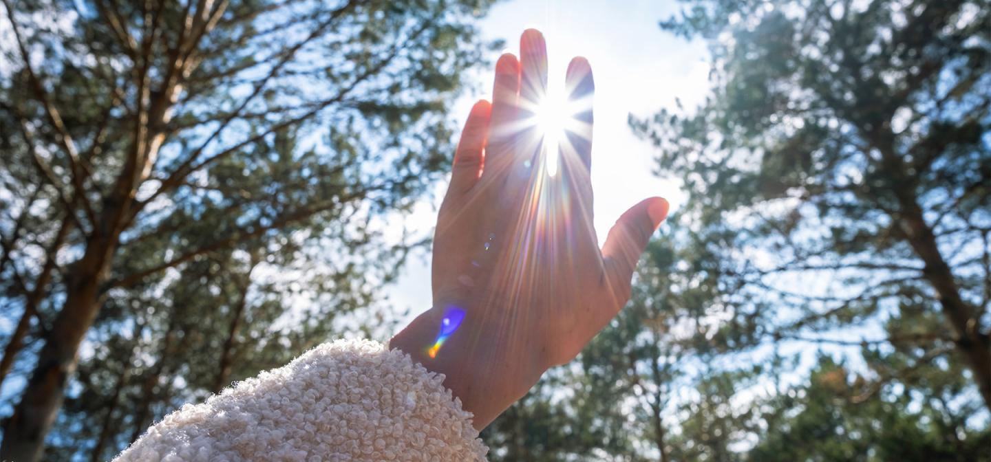 Person reaching towards the sun, with the light filtering through their fingers, symbolizing a connection with spirituality