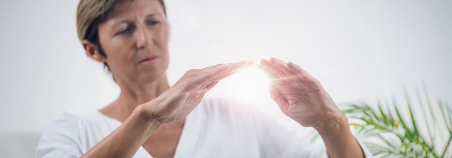 Woman practicing energy healing and mindfulness meditation with glowing light between hands symbolizing holistic wellness.