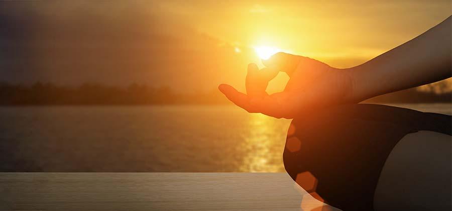 Person meditating on a dock at sunset