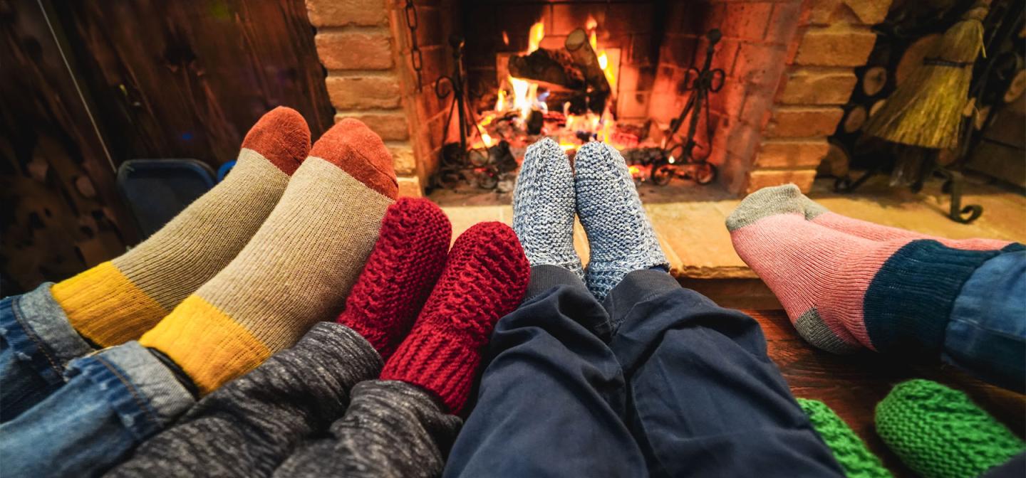 Cozy sock-covered feet gathered by a warm fire, symbolizing comfort and connection as winter days grow shorter.