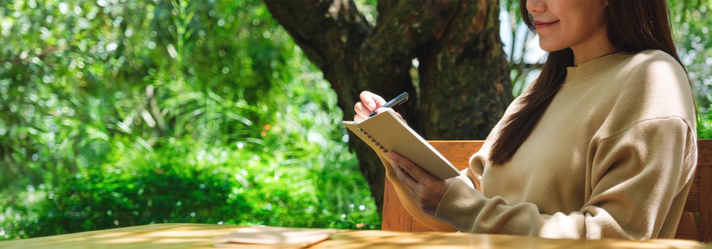 Person journaling outdoors in a peaceful garden setting during a writing for healing retreat focused on self-discovery, reflection, and creative expression.