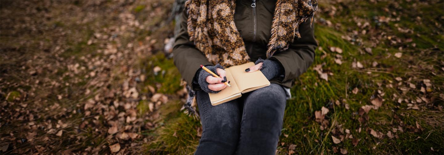 Person writing in a journal outdoors during a symbolizing memoir writing and creative storytelling