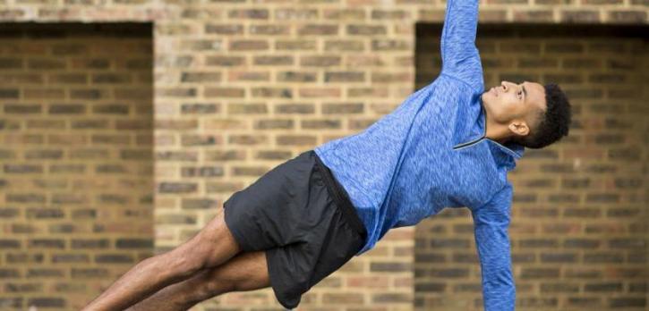 Man practicing yoga side plank pose outdoors, promoting yoga workshops and retreats at Omega Institute.